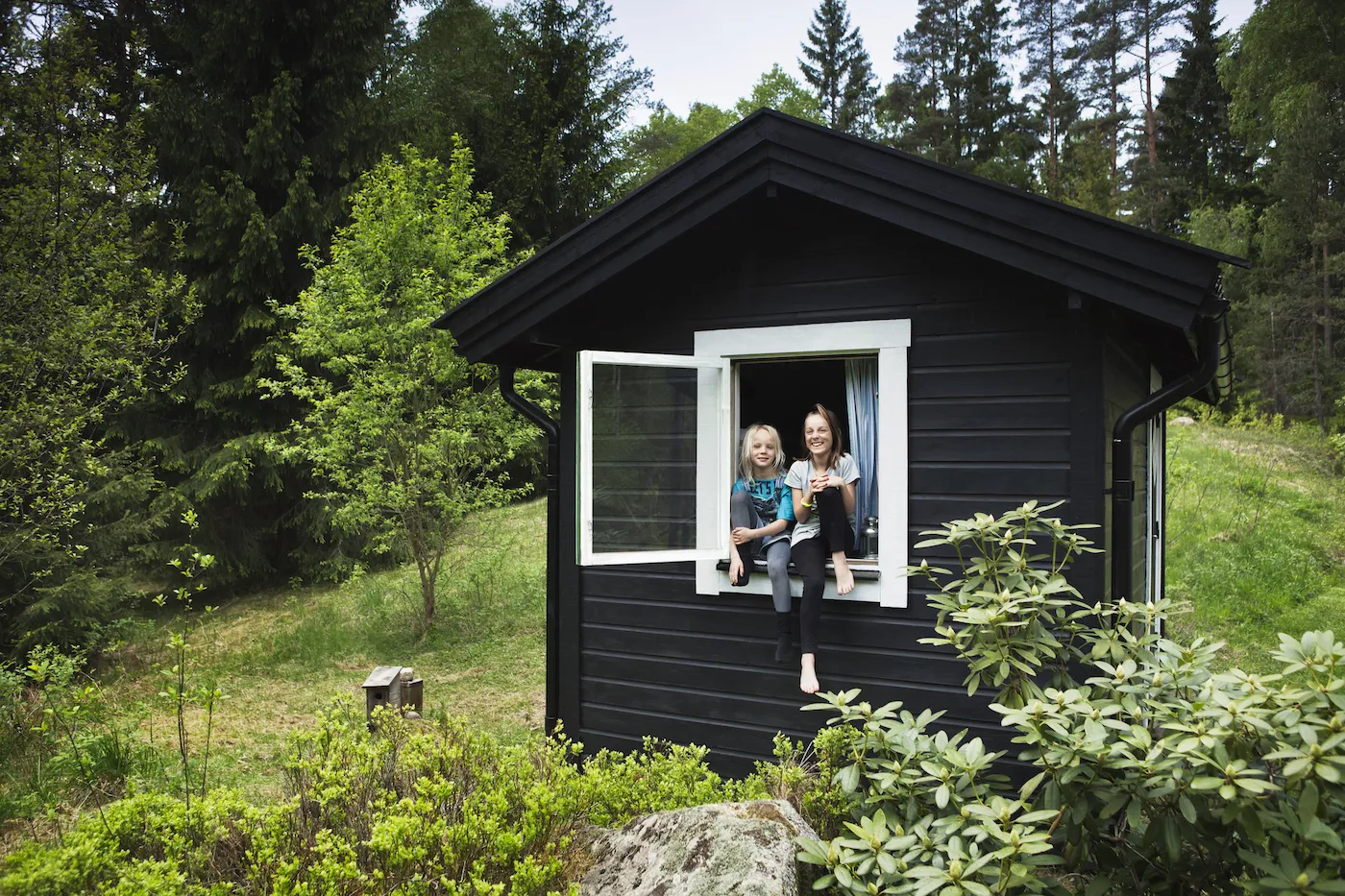 Girls sitting in window of tiny house in lush green PNW backyard