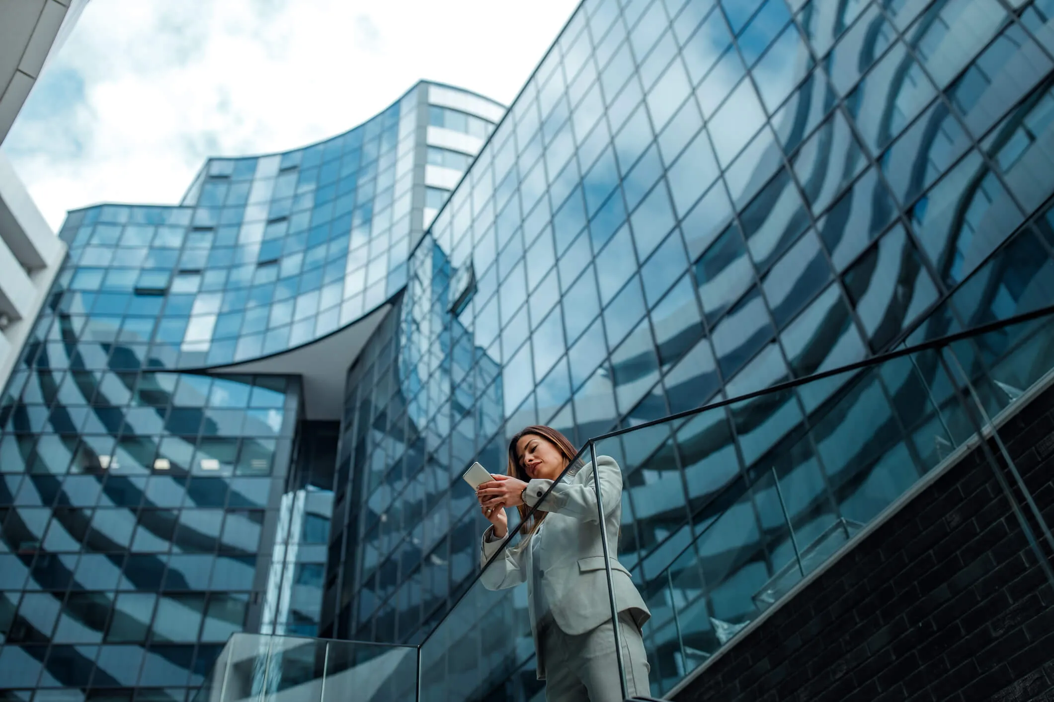 Business woman using her phone while standing next to a large office building