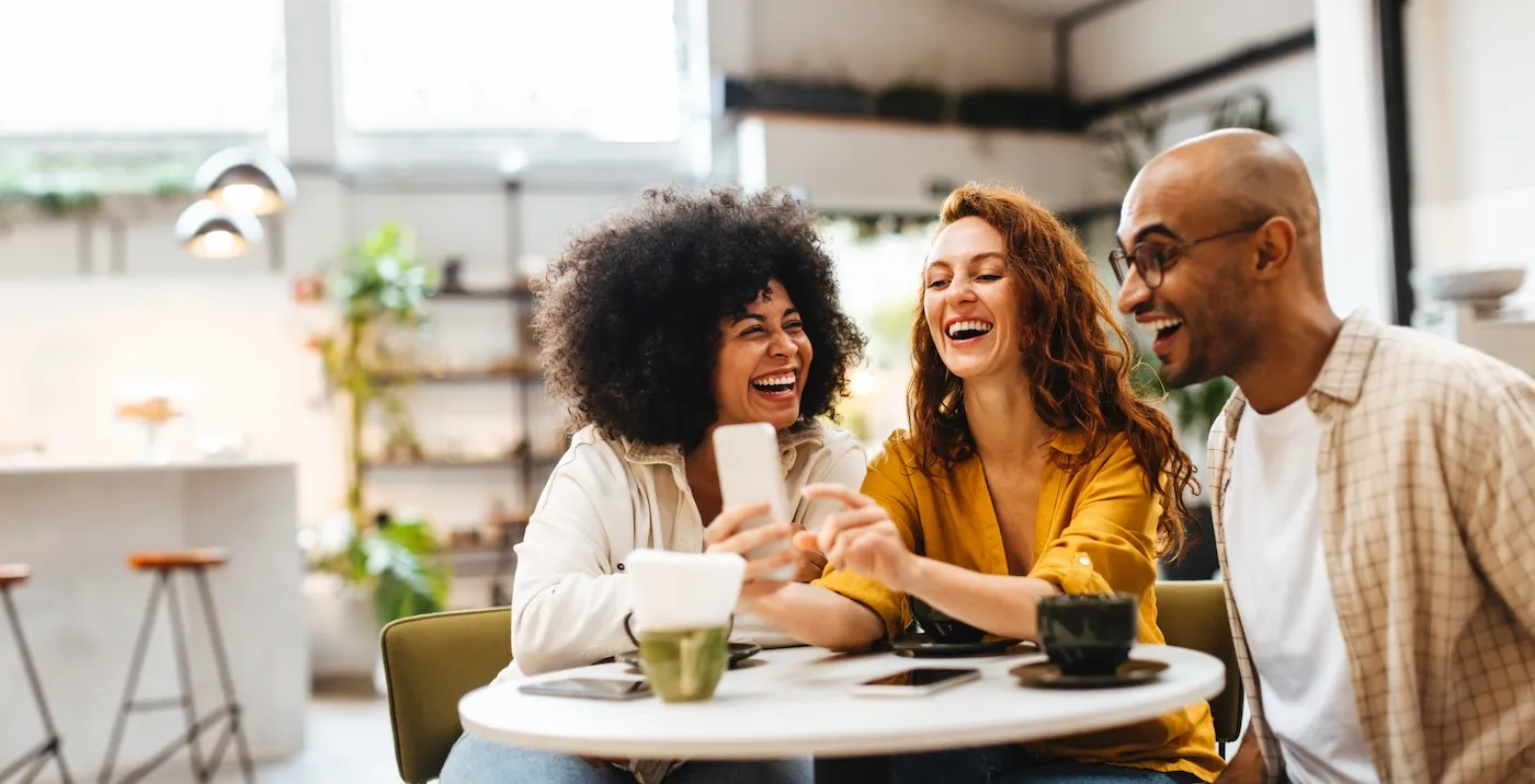 Group of happy friends browse social media on a smartphone in a lively cafe.