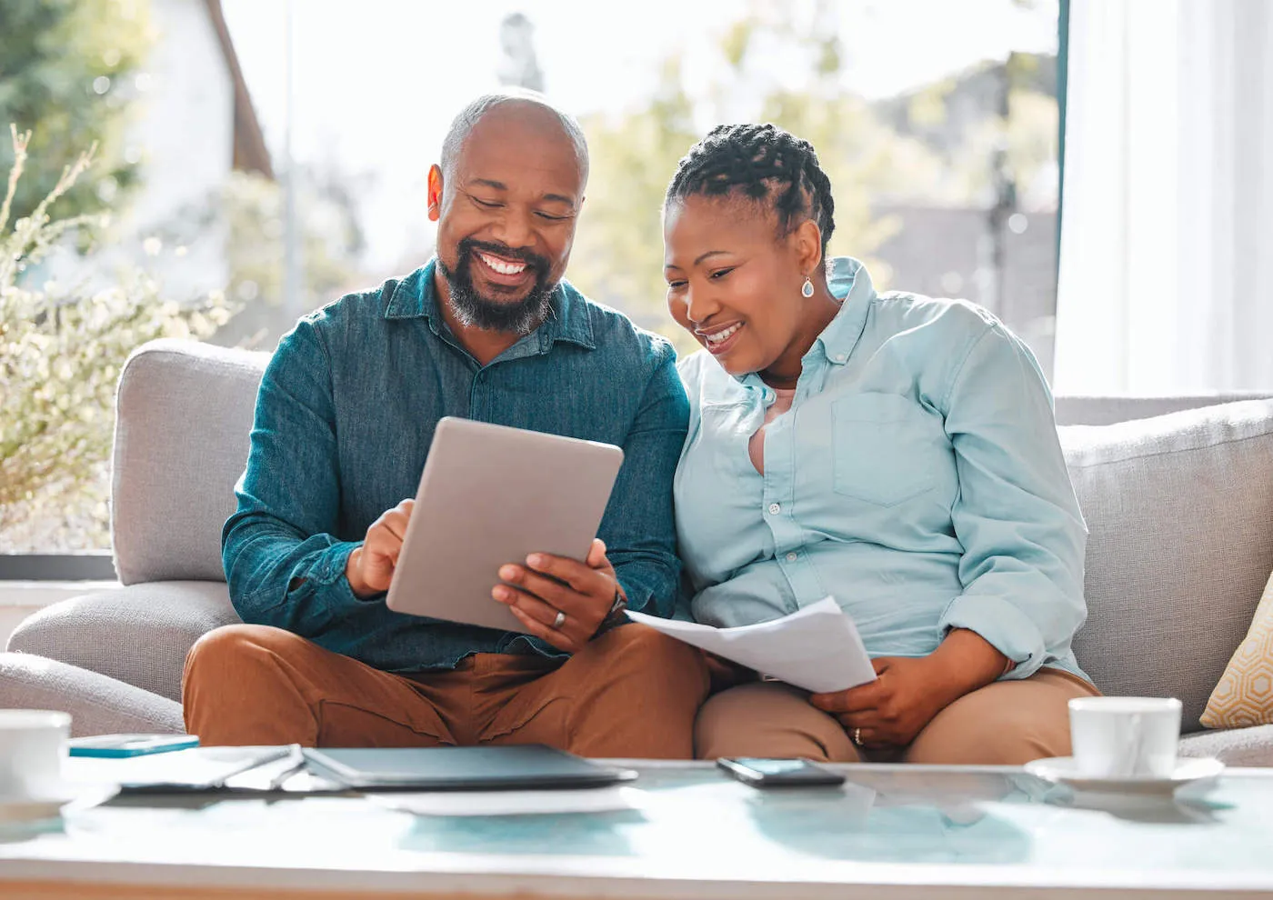 Man and woman couple seated on sofa looking up bank rates on tablet device.