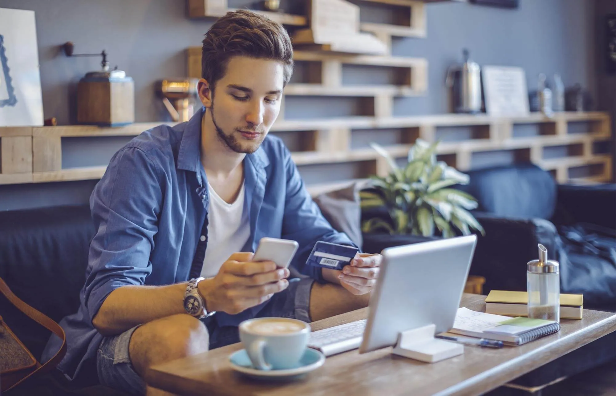 A man checking his phone and holding a credit card in a coffee shop