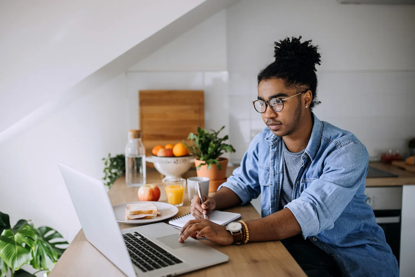 Young casually clothed man checking finances on a laptop from his kitchen.