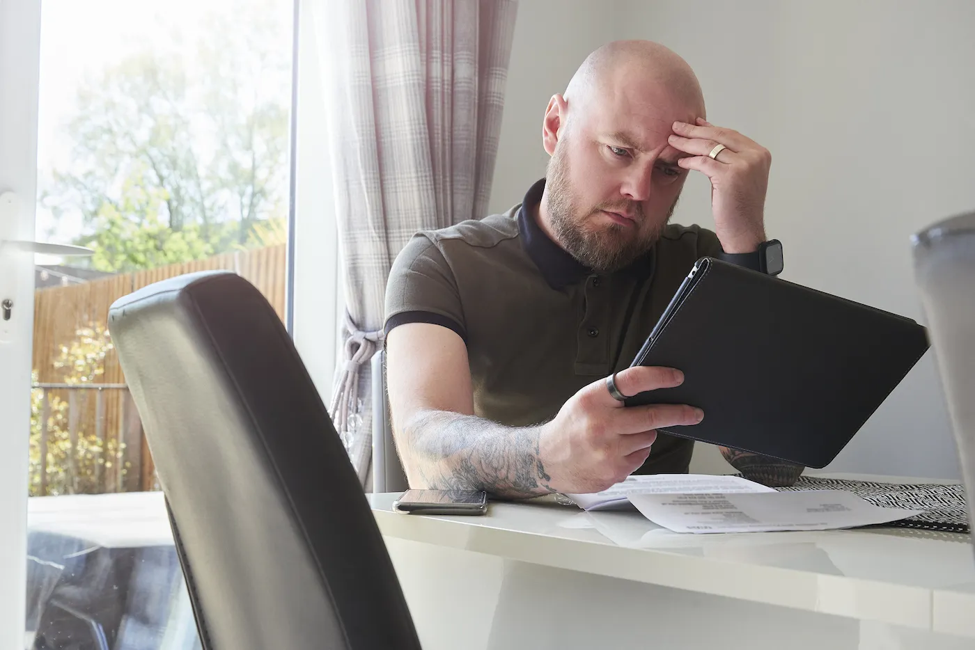 A male homeowner sits at the dining table considering refinancing his home to pay debts.