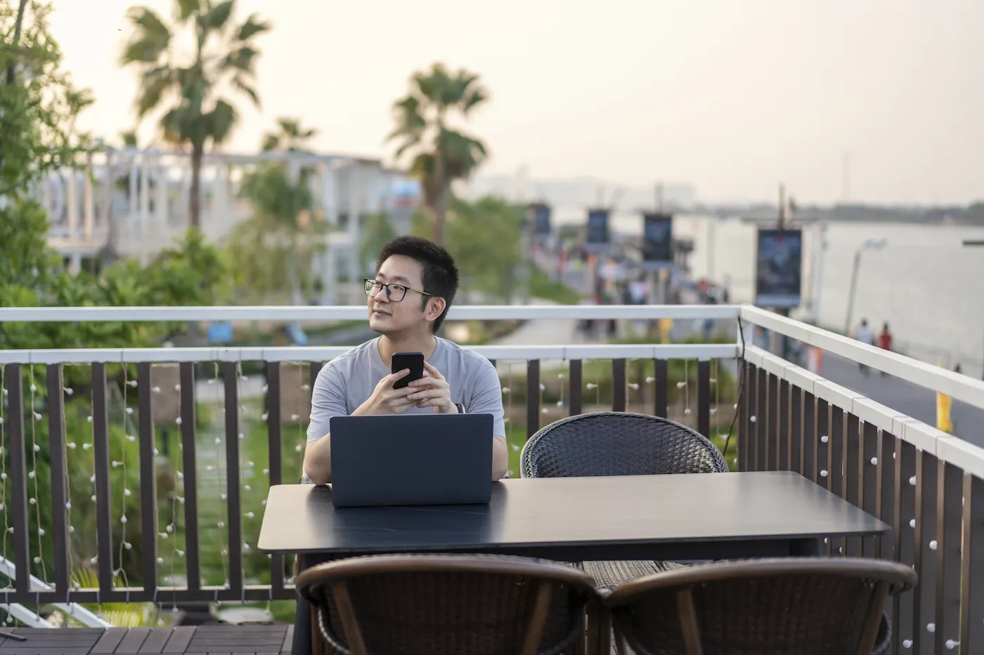 Man sitting outside at a table on a patio in front of his laptop, holding his phone and wondering how safe high-yield savings accounts are.