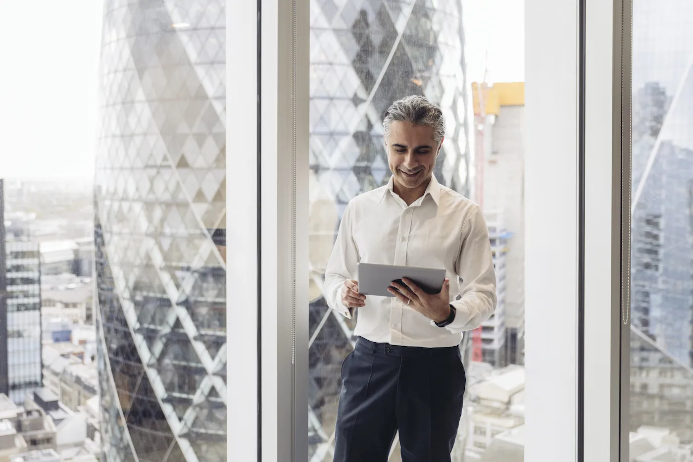 Man standing in an office checking his savings account on a digital tablet.