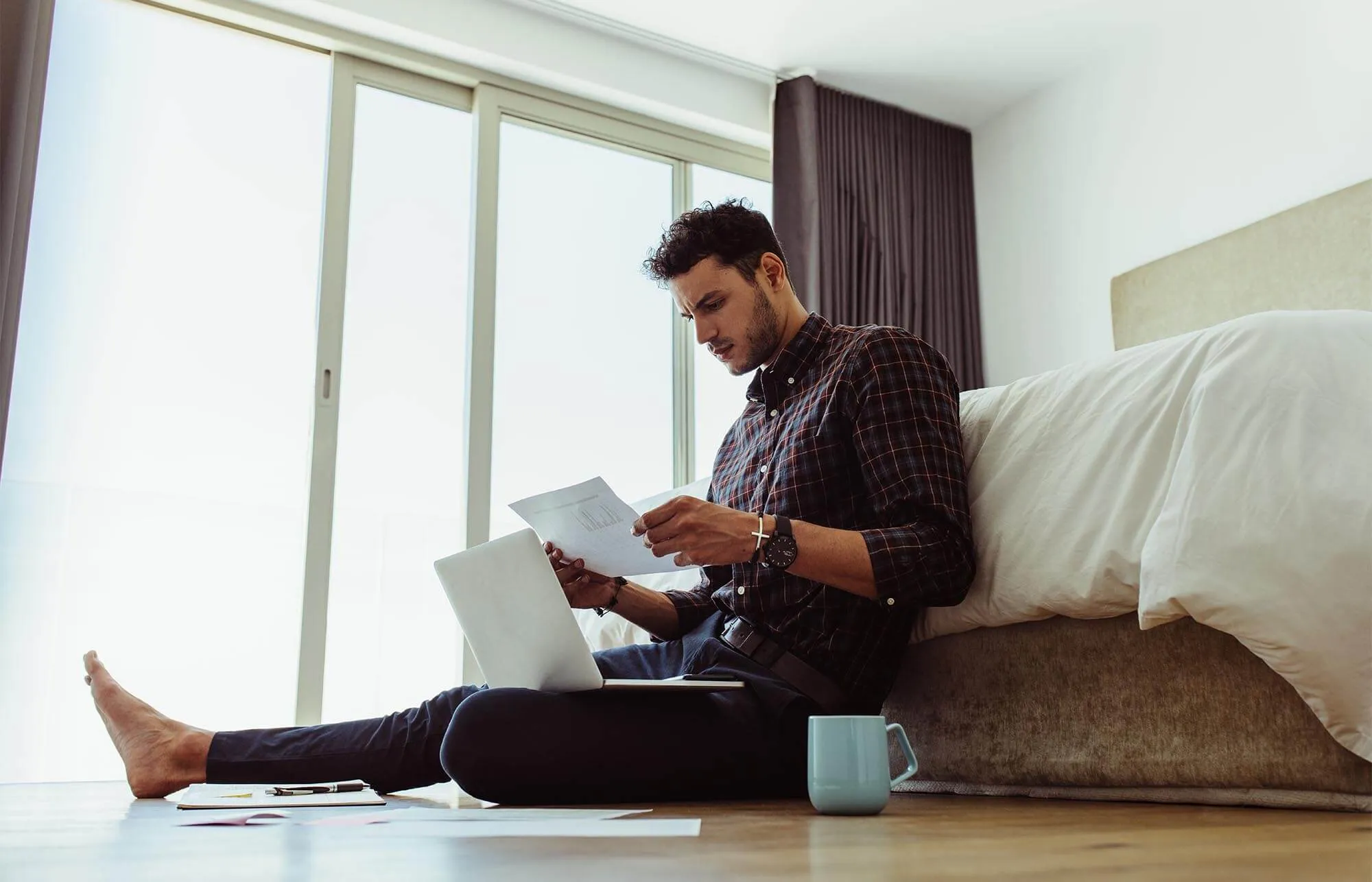 A man looking at papers on the floor of his bedroom