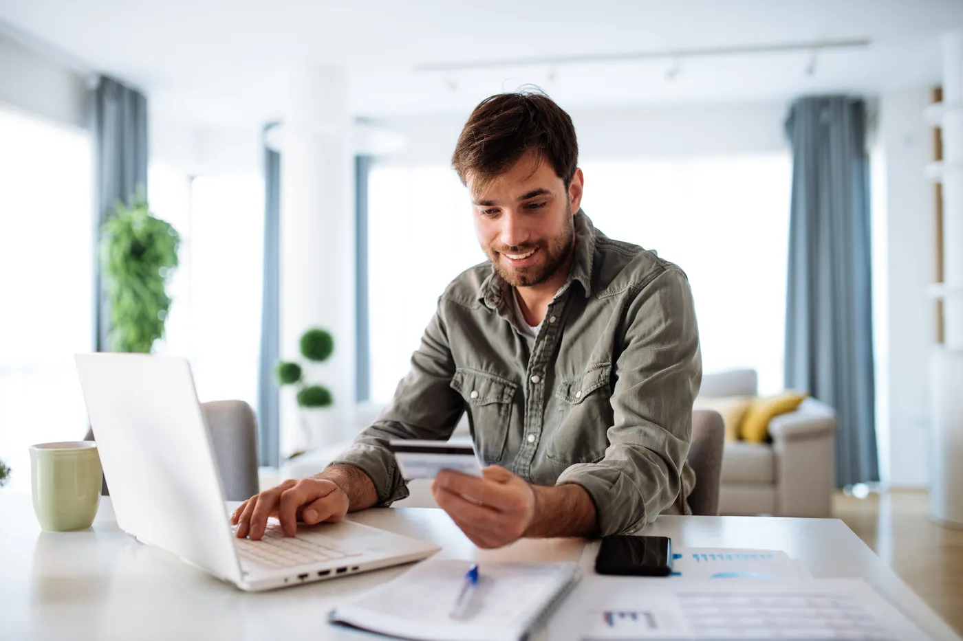 Man putting deposit on secured card, smiling holding card and using laptop.