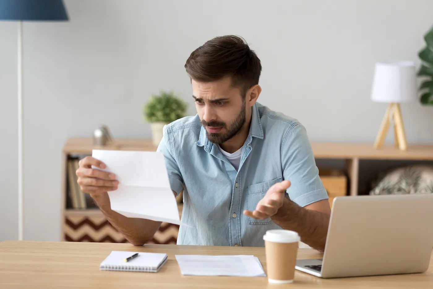 Confused frustrated young man holding mail letter reading bad news that he was denied a personal loan