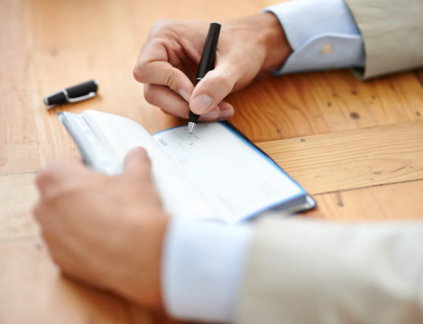 Cropped closeup shot of a man writing in a checkbook