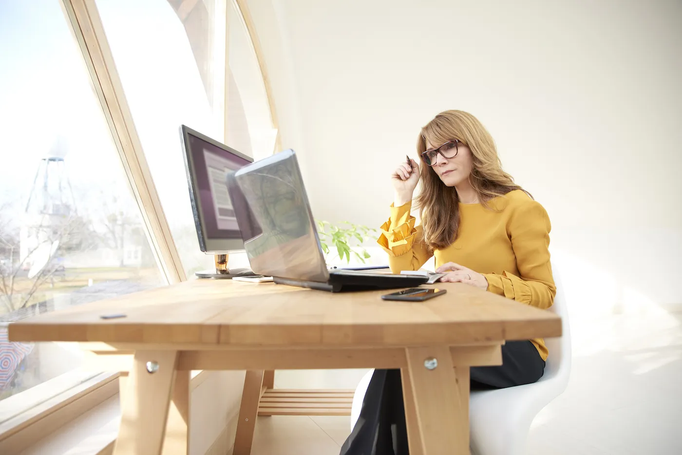 A woman looking thoughtful while sitting at computer and laptop, researching money market and CD accounts in her home office.