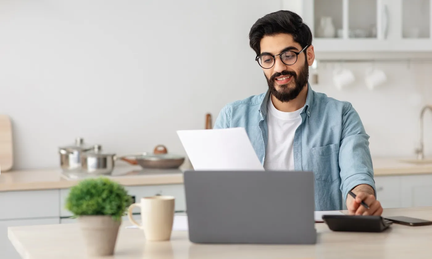 Portrait of a man reading a paper document and sitting at a laptop.