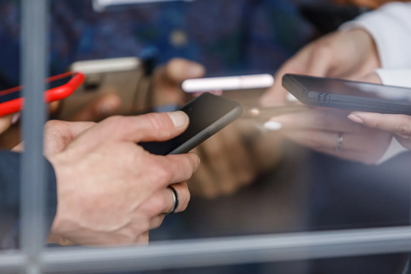 Close up shot of unrecognizable group of business people standing by the window, using their smart phones, initiating payments. Seen through glass window.