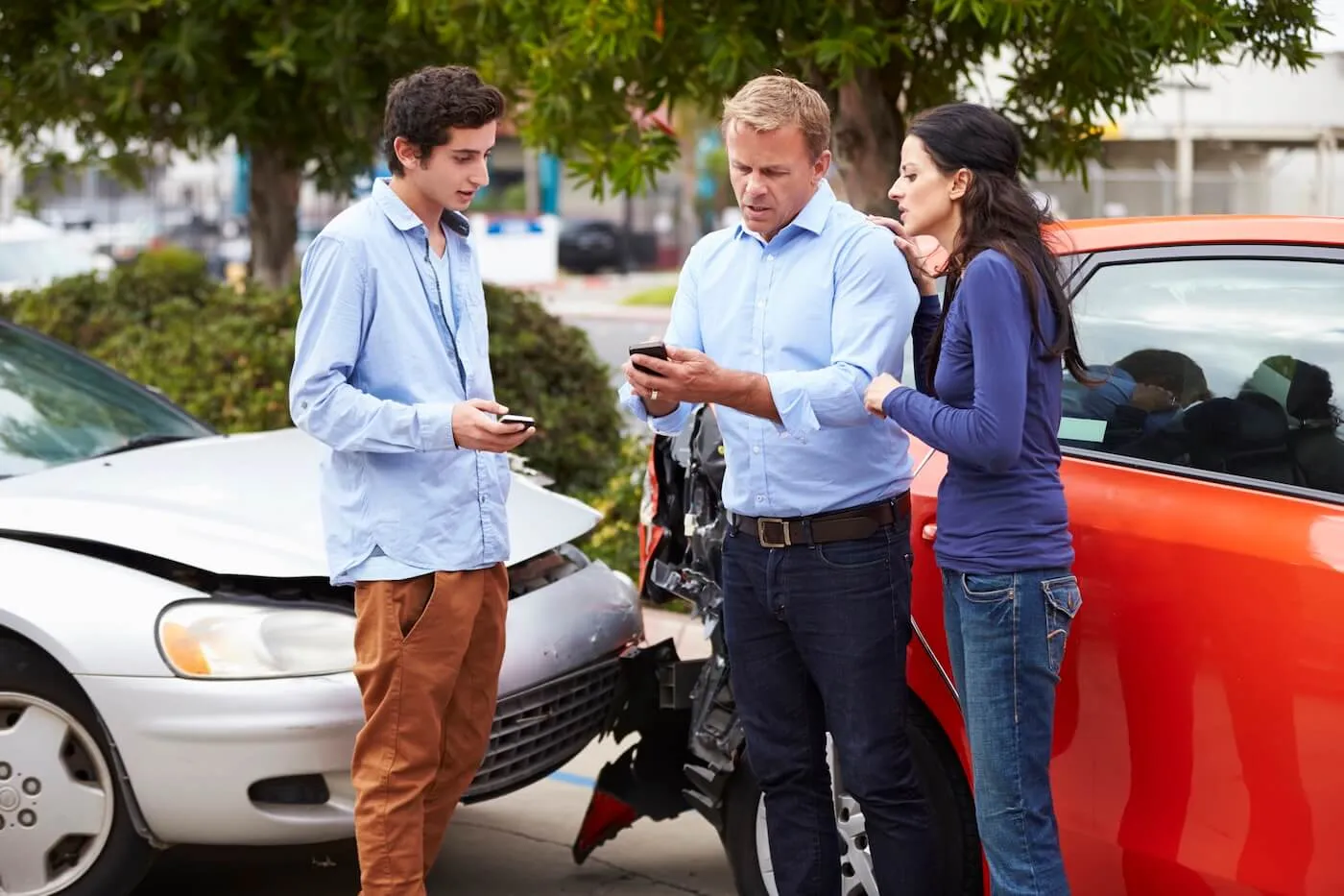 A woman and two men exchanging contact information while standing next to collide cars