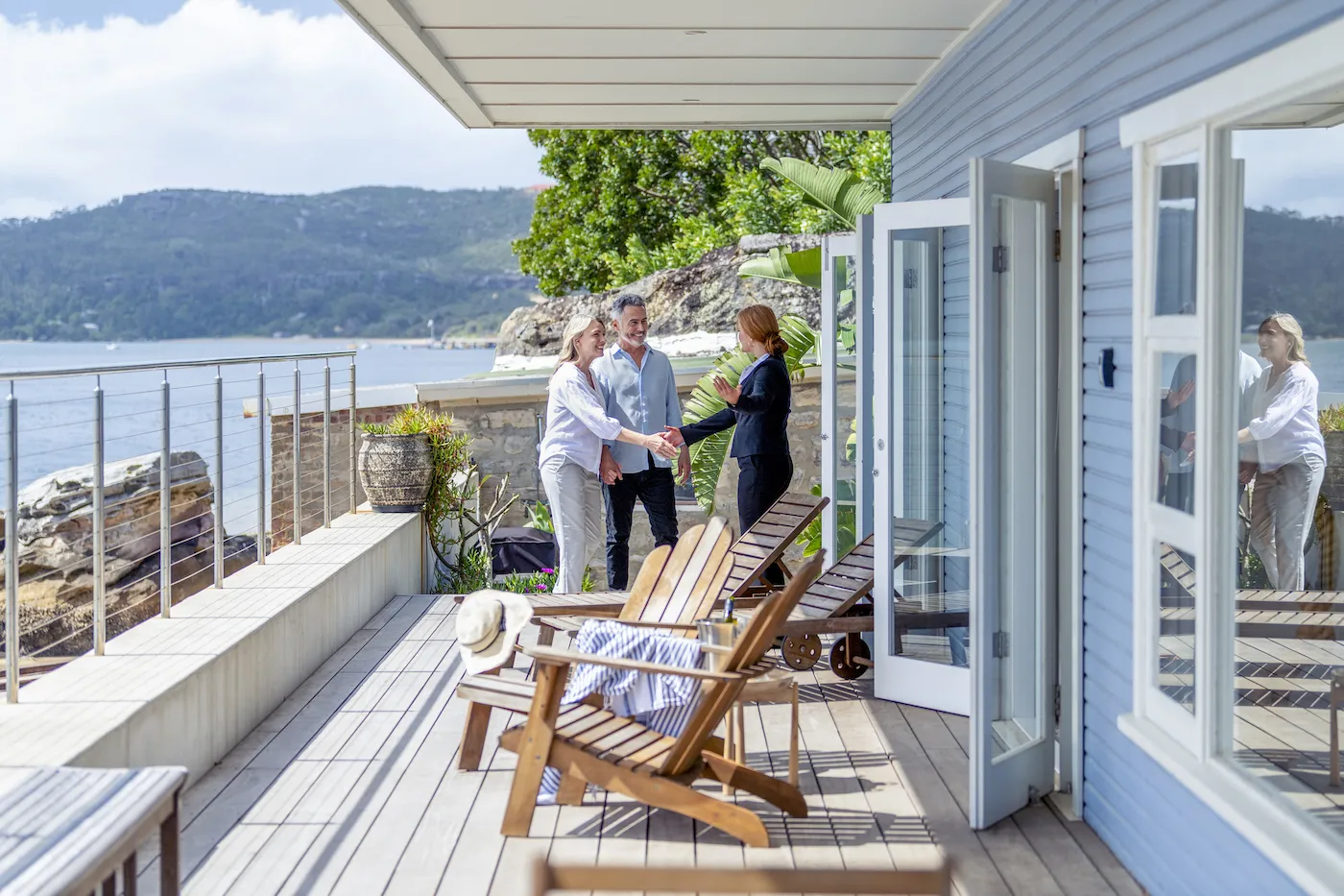 Oldder couple meets agent on deck of waterfront house.