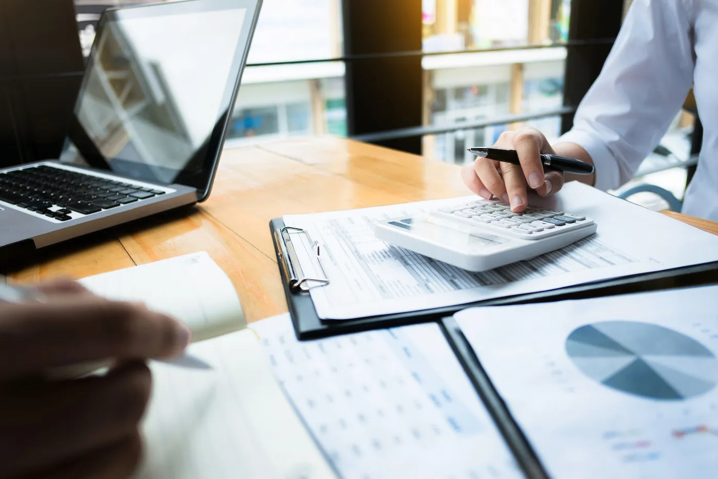 A person's hang using a calculator on a desk with papers, calculating income taxes