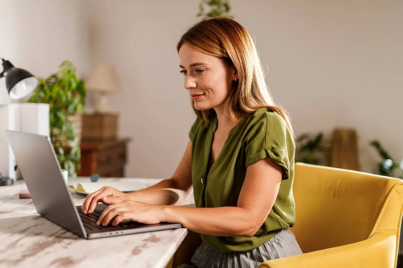 Smiling woman is using her laptop in a sunny home office