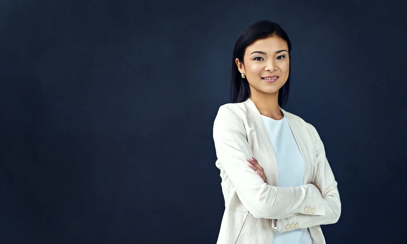 Portrait of a smiling asian woman with crossed arms against a dark background.