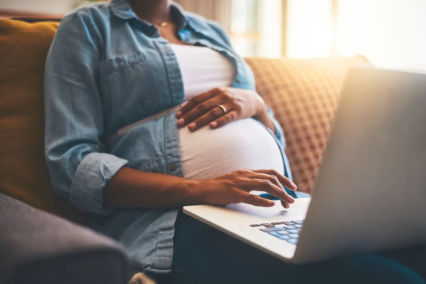 Cropped shot of a pregnant woman sitting on the couch using her laptop at home