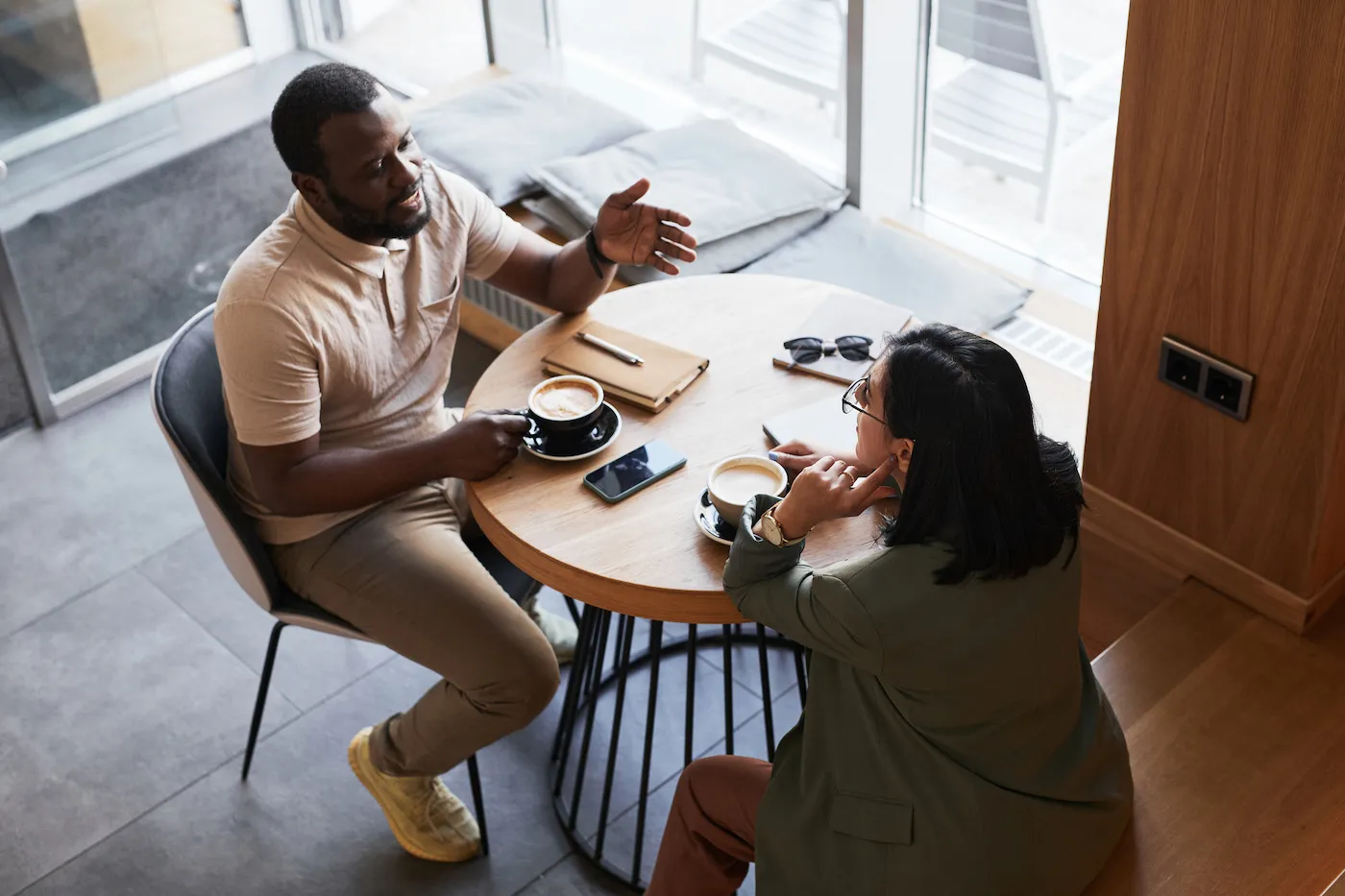 High angle portrait of two young people chatting at table in graphic cafe interior.