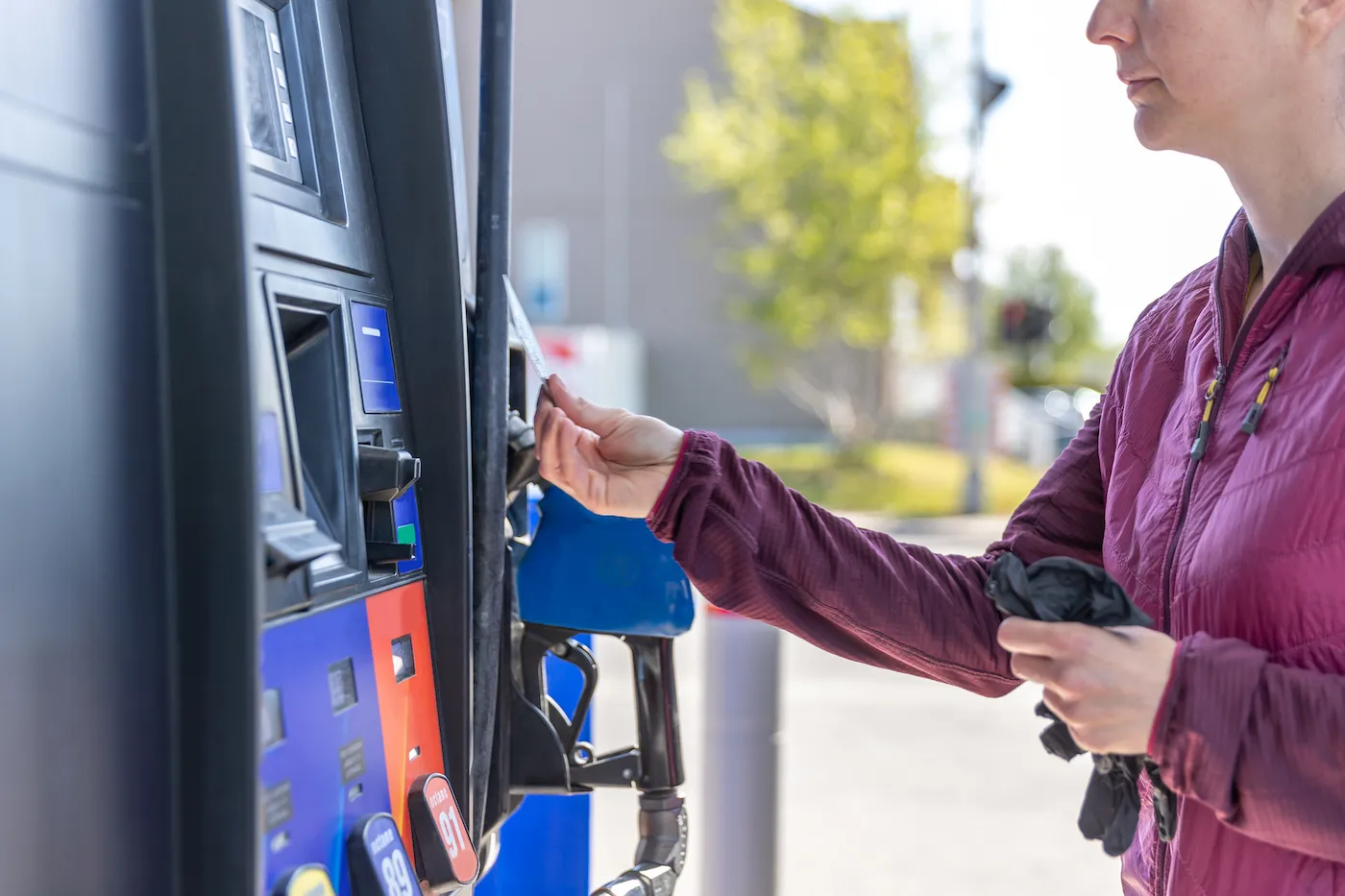 A woman is paying at the fuel pump at the gas station with a card.