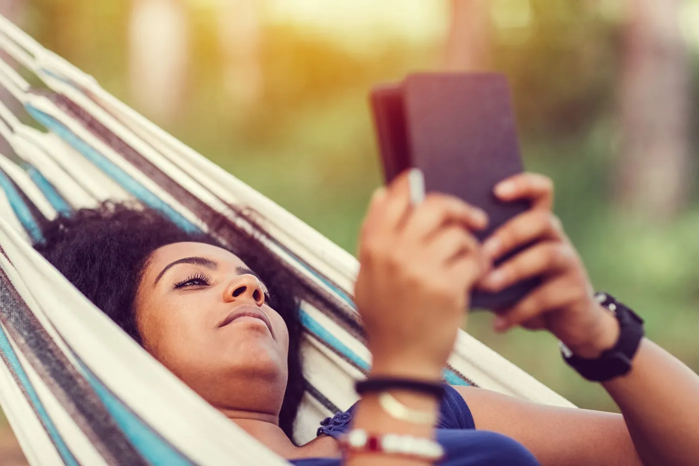 A woman reading her ebook while laying in a hammock.