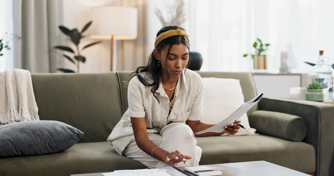 Woman sitting with a calculator and her budget on sofa, figuring out her home insurance.