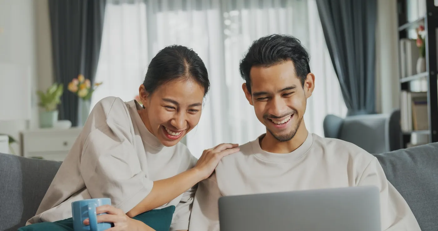 Happy young couple sit on couch fun use laptop computer setting up a HYSA at home.