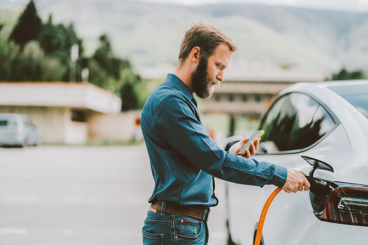 A man charging his electric car while looking at his phone