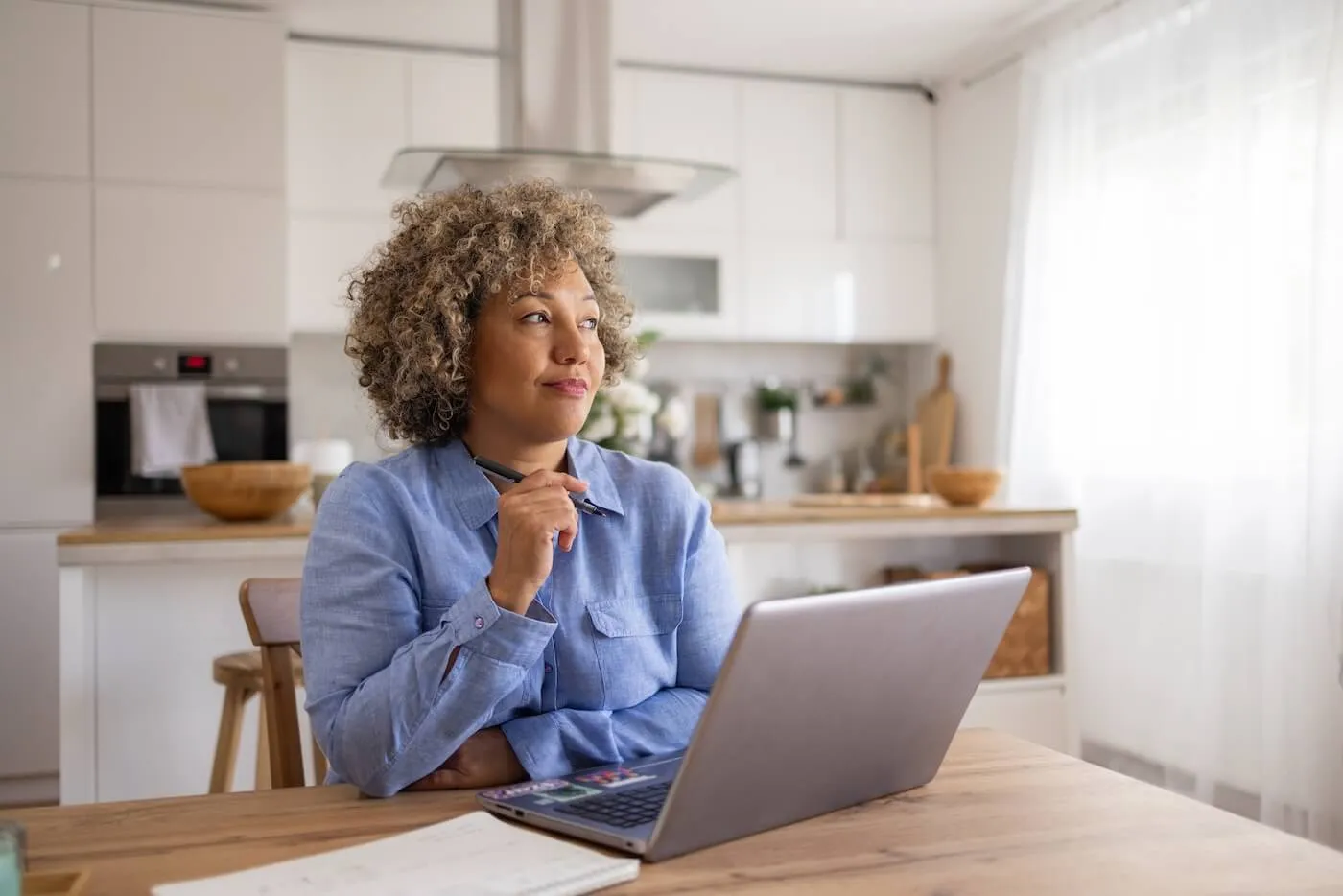 Thoughtful woman sitting in kitchen in front of an an open laptop