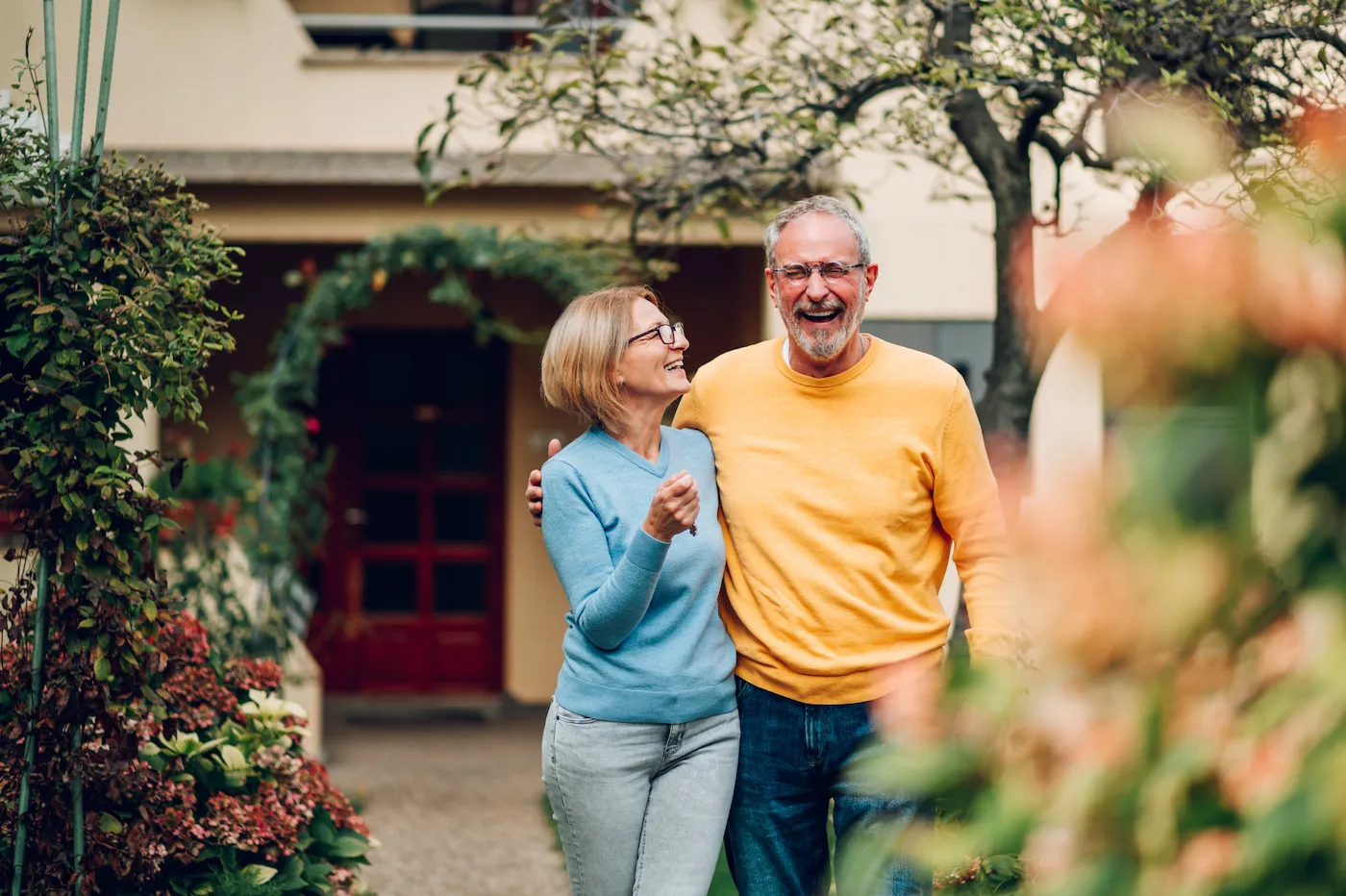 Portrait of a senior married couple holding keys and standing outside their new home on a moving day and hugging.