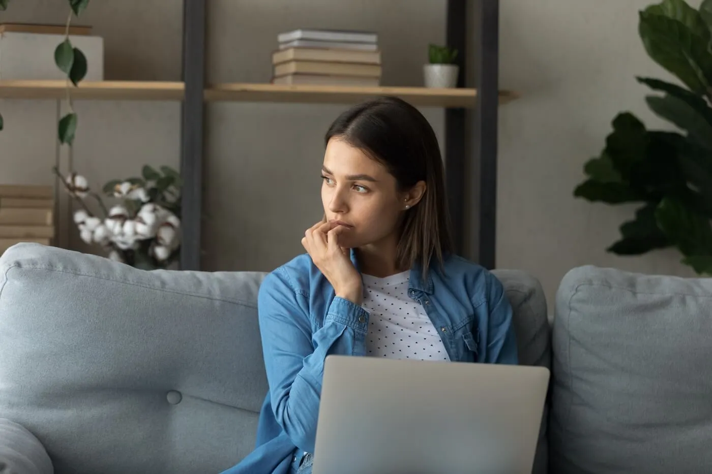 Woman thinking while sitting on a couch with a laptop