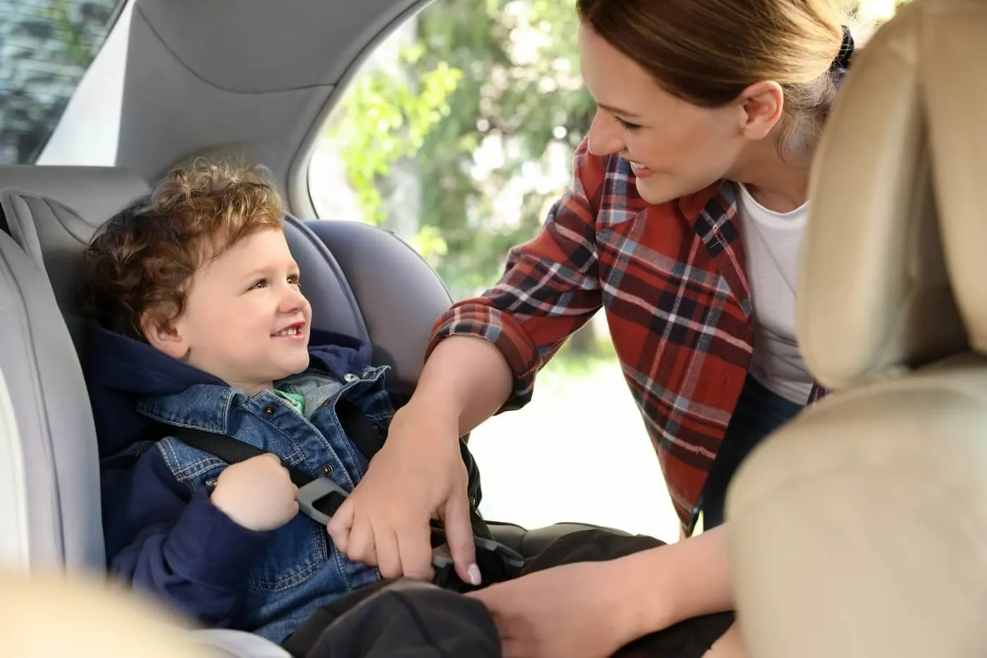 Happy mother buckling up a smiling toddler boy in a car seat