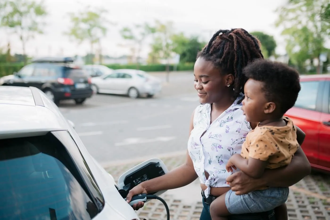 Young woman holding a toddler while charging her electric vehicle