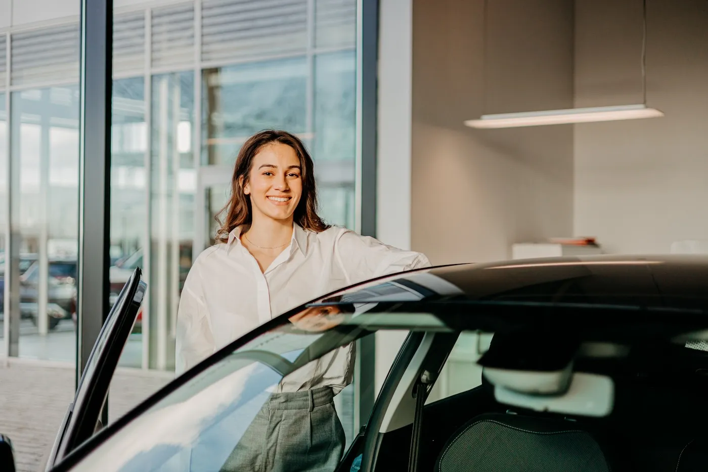 Standing next to the car, a woman looks directly at the camera.