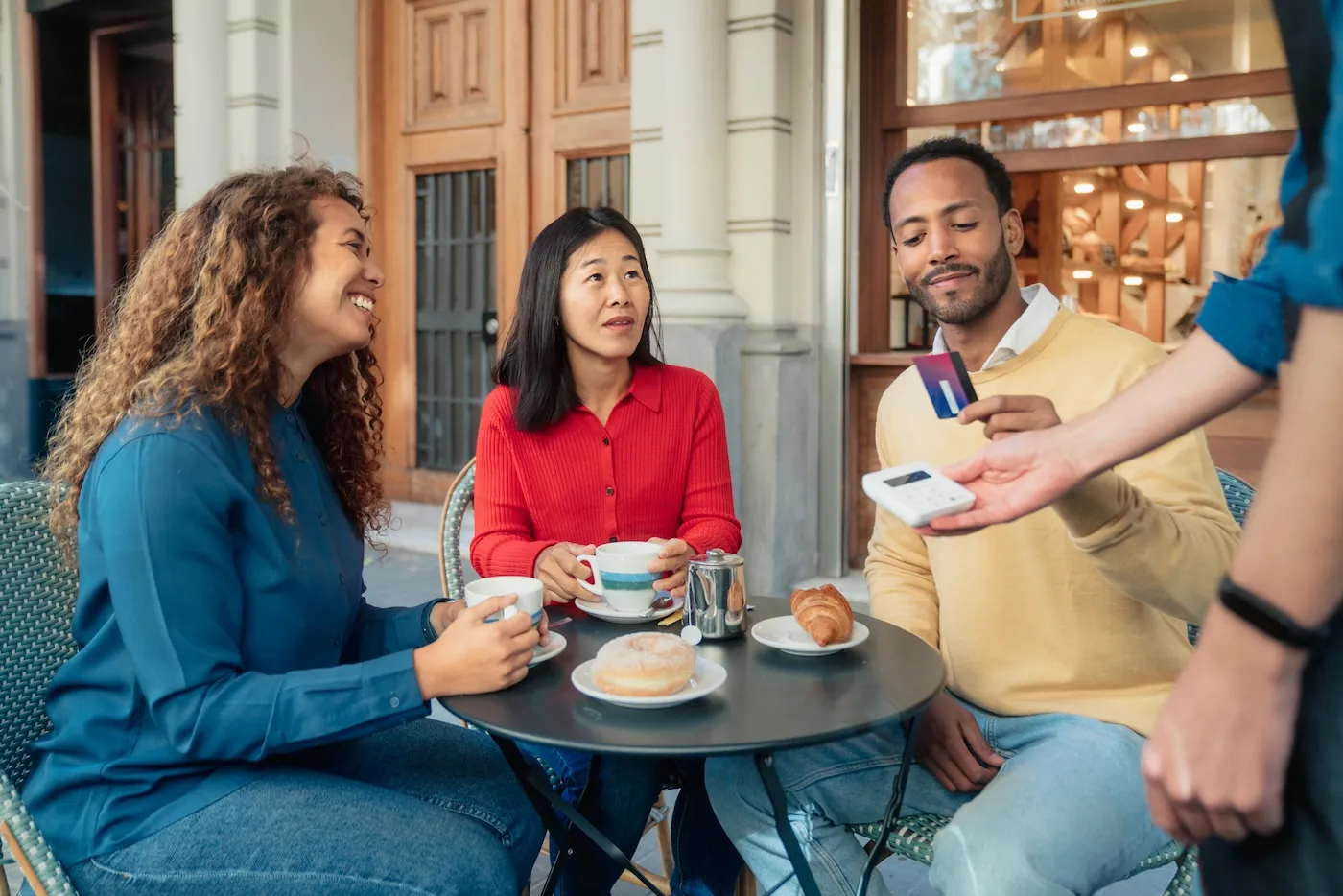 Friends paying using contactless payment with credit card at an outdoor cafe in Barcelona.