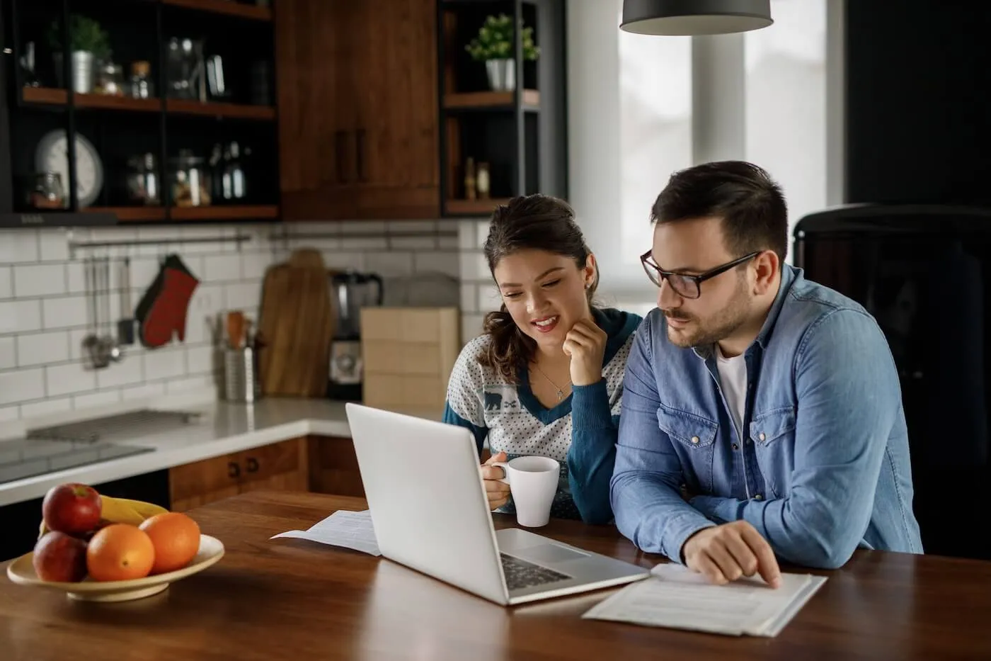 Couple checking online auto loan terms on their laptop while having tea in their kitchen