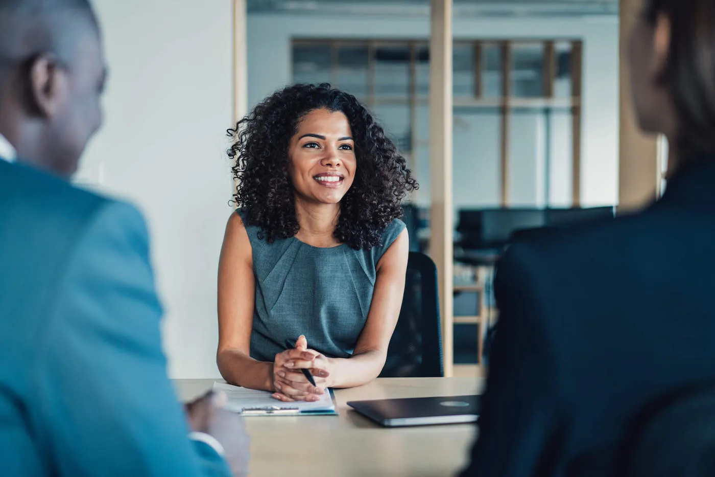 Smiling woman conversing with male and female couple in business setting.