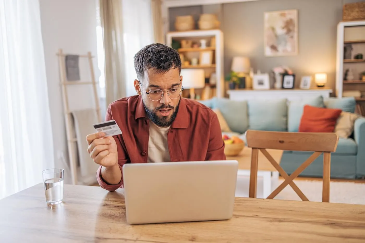 Concerned man using his laptop in the living room while holding his credit card