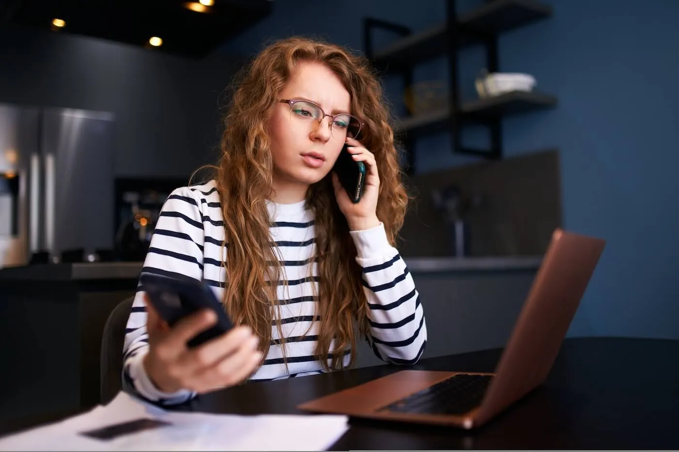 Concerned young woman is making a phone call while using her laptop