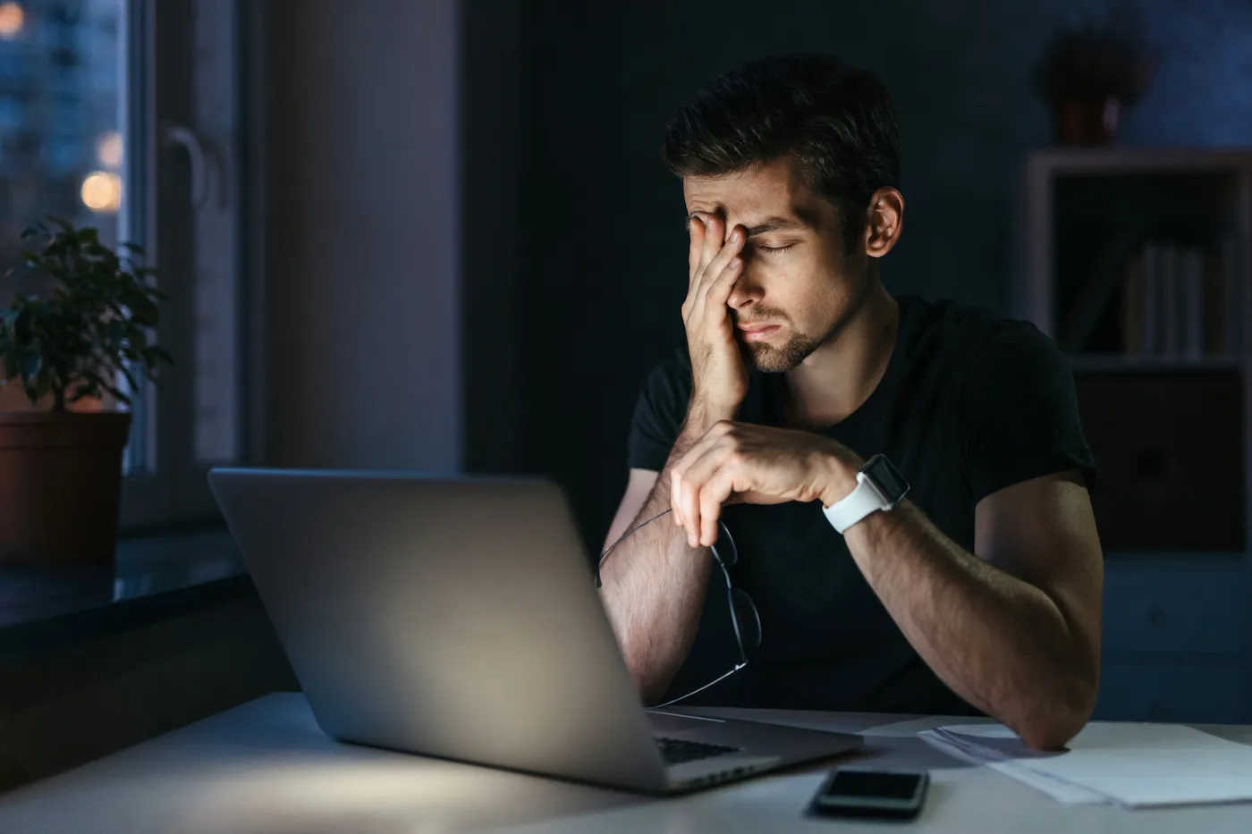 Stressed tired man rubbing his eyes staring at his laptop, coping with the burden of debt.