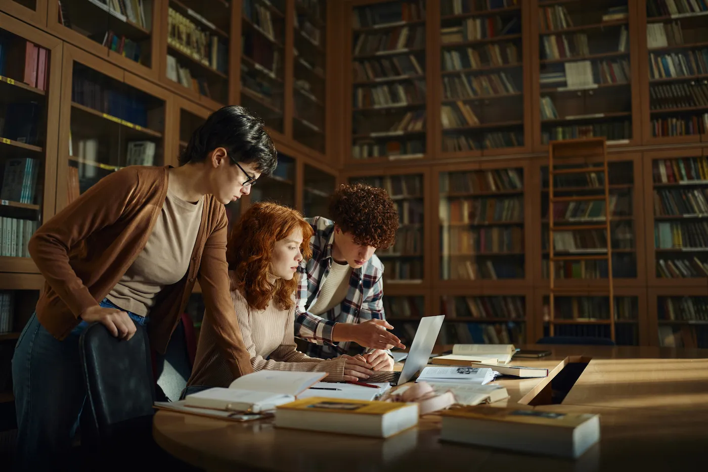 Group of students cooperating while e-learning over a computer and books in library.