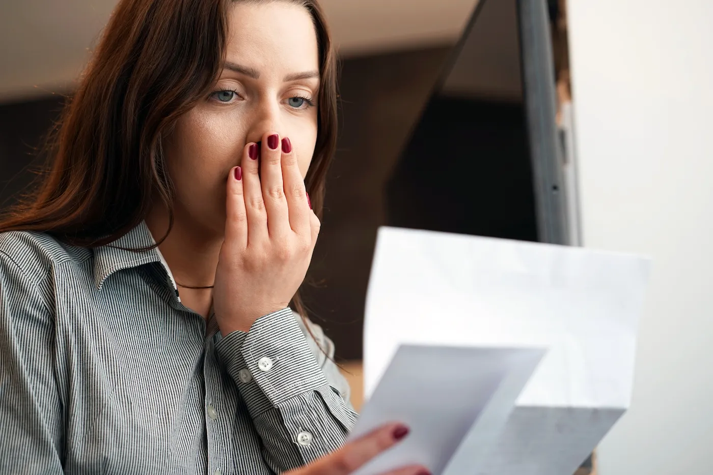 Surprised woman realizing the harmful effects of identity theft as she reads a letter with bad news.