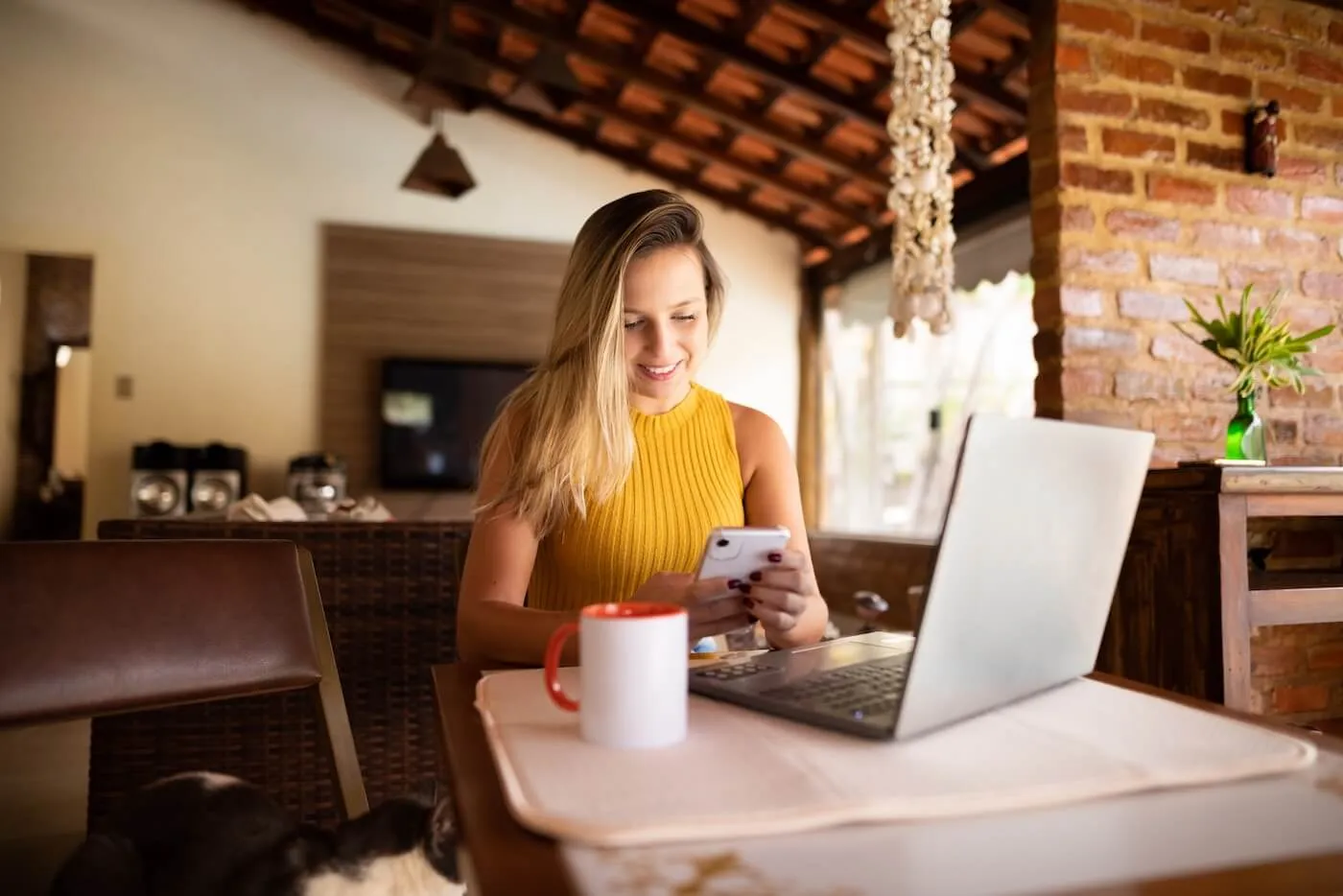 Young woman is using her mobile phone and a laptop in a sunny living room