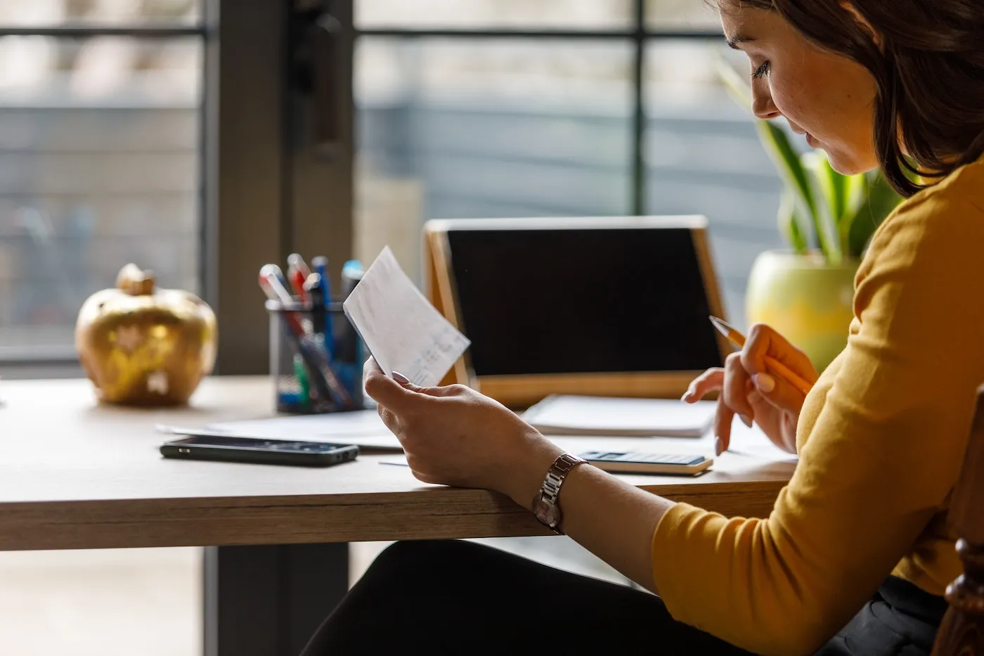 A young woman sitting at home office desk, using a calculator and sorting out various finances and bills.