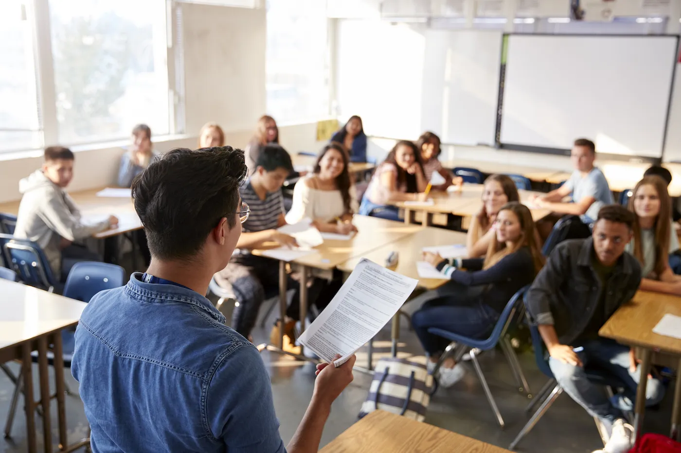 High school teacher holding notes in front of the class.