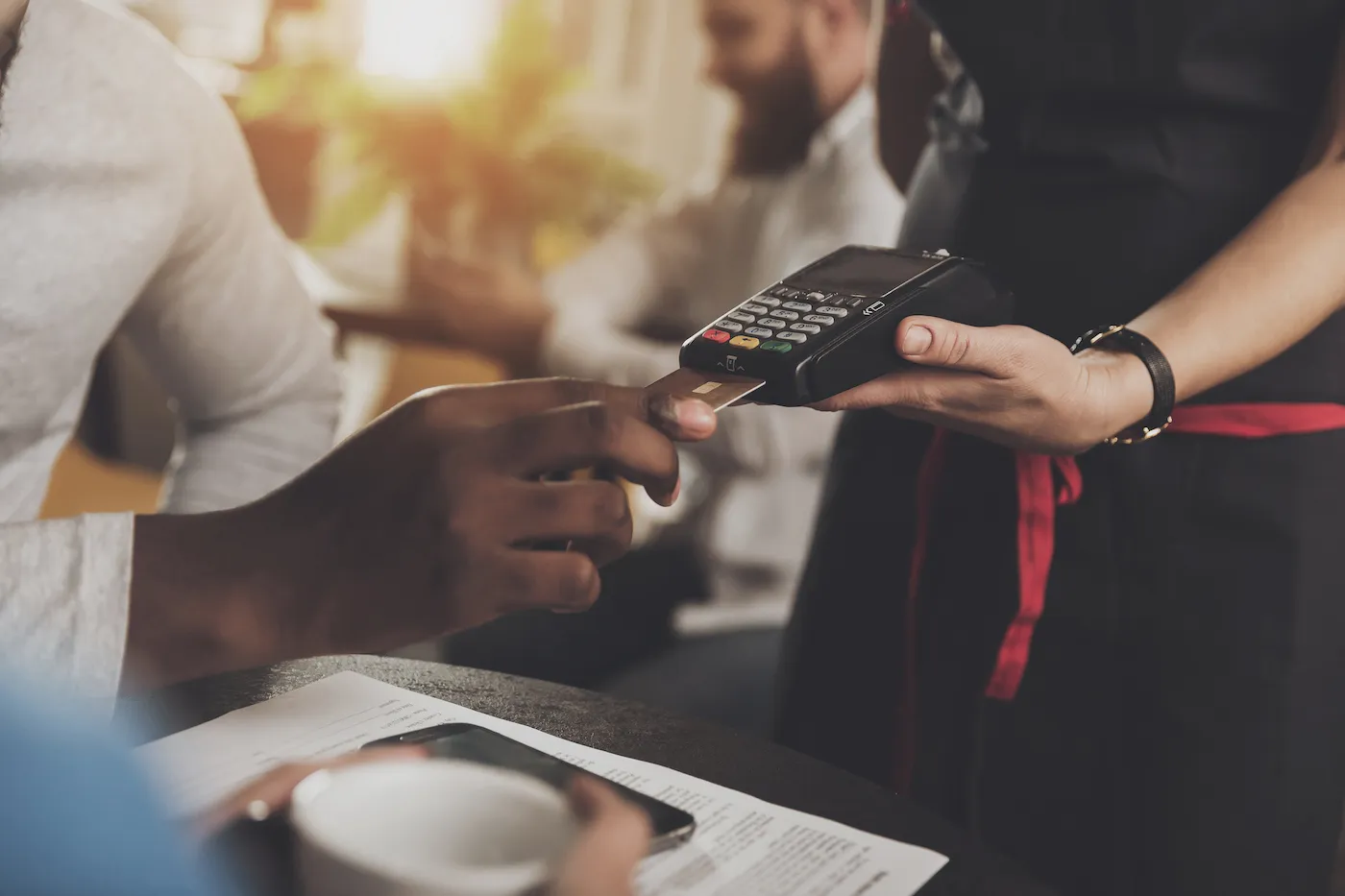 A person's hand holding a credit card up to an electronic point-of-sale device at a café.