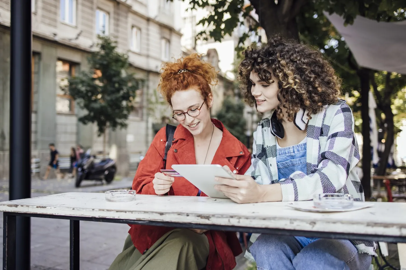 Two women spending time at the sidewalk cafe and shopping online together.