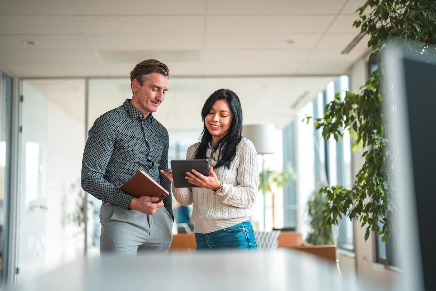 A man and a woman standing in a house, looking at a digital tablet to figure out how to pay debt.