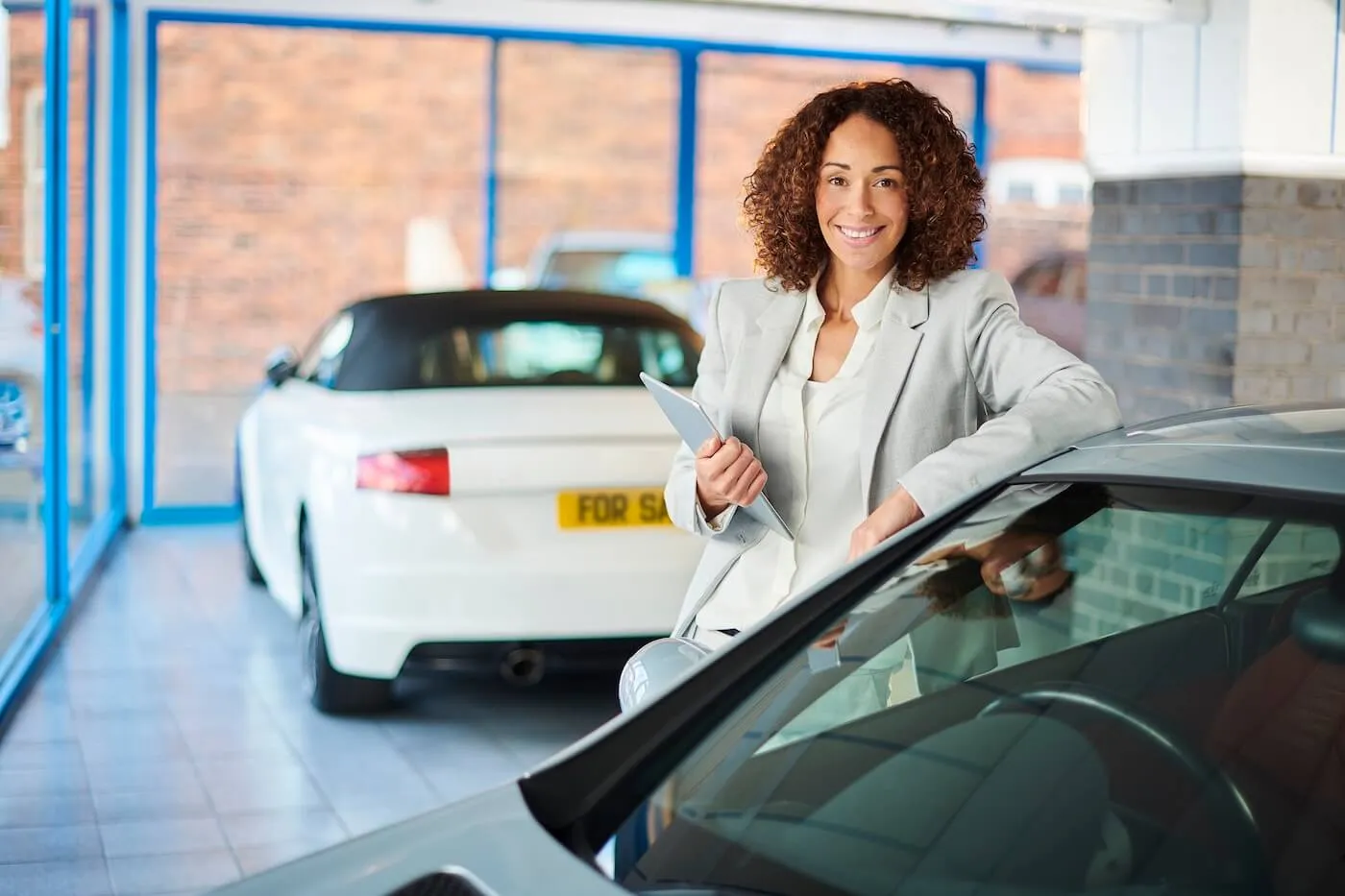 A photo of a smiling female agent standing next to a car in a dealership showroom