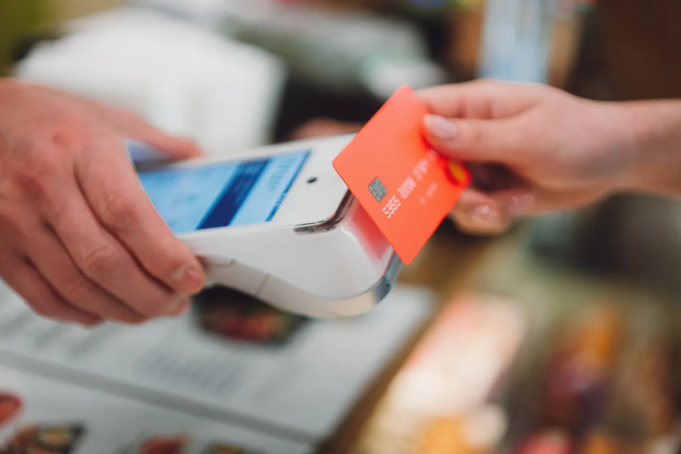 Close-up shot of woman paying at a credit card reader with a contactless credit card to avoid a card skimmer.